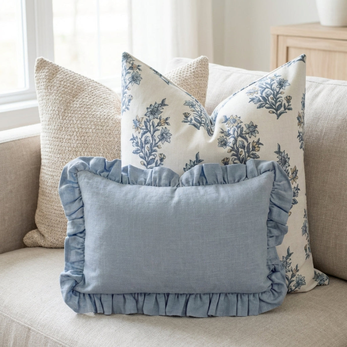Close-up of Ronan Sofa Combo 5 pillows with woven, floral, and ruffled details on a neutral sofa in a bright, airy environment.