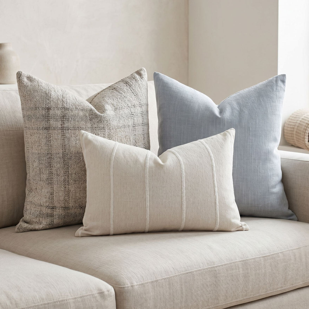 Neutral-toned sofa adorned with Bennett sofa combo pillows, featuring coastal blues, plaid, and textured stripes in a serene living space.