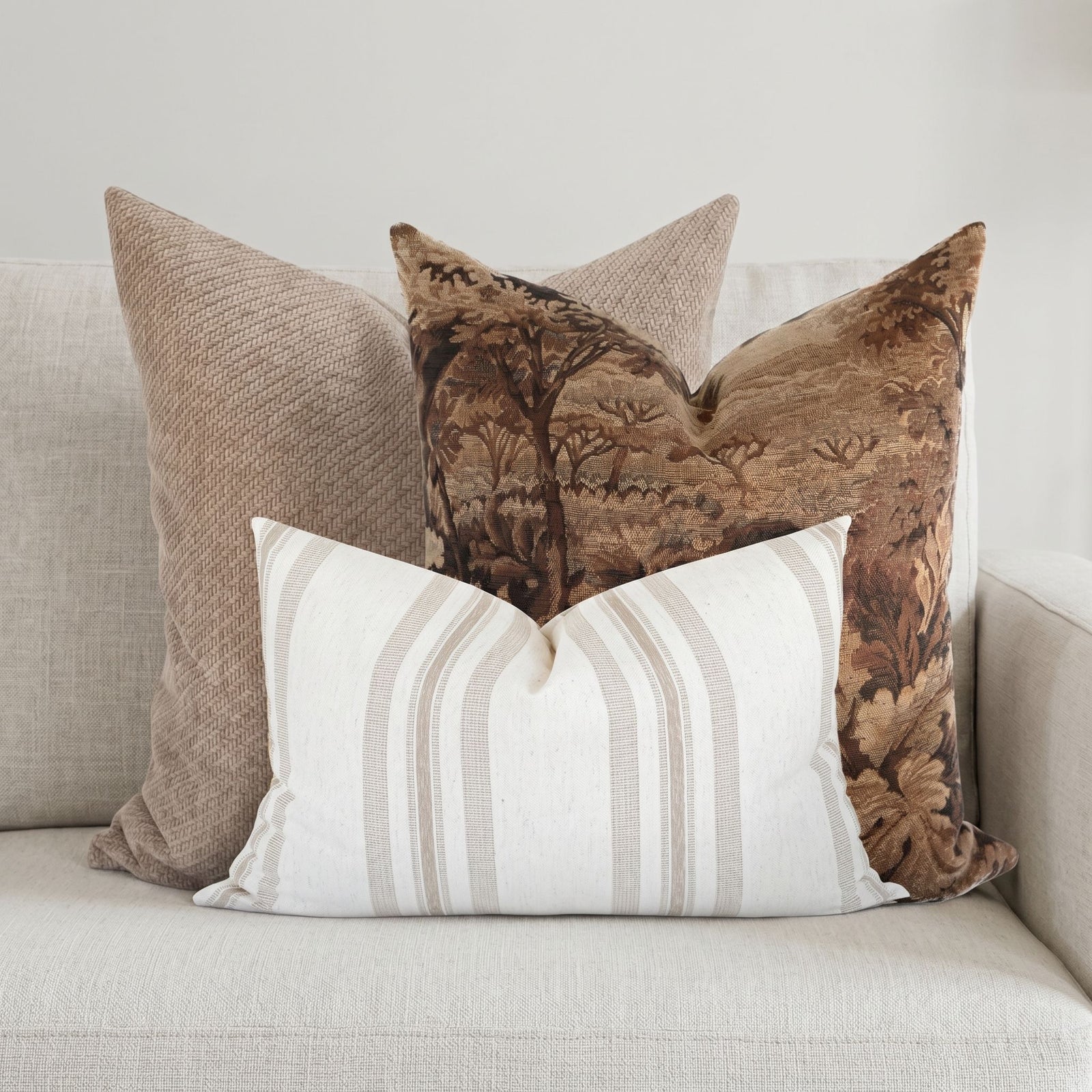 Pillow set on a neutral-toned sofa in airy living room, featuring woodland Finnegan tapestry, warm Banks weave, and striped Quincy for elegant, cozy decor