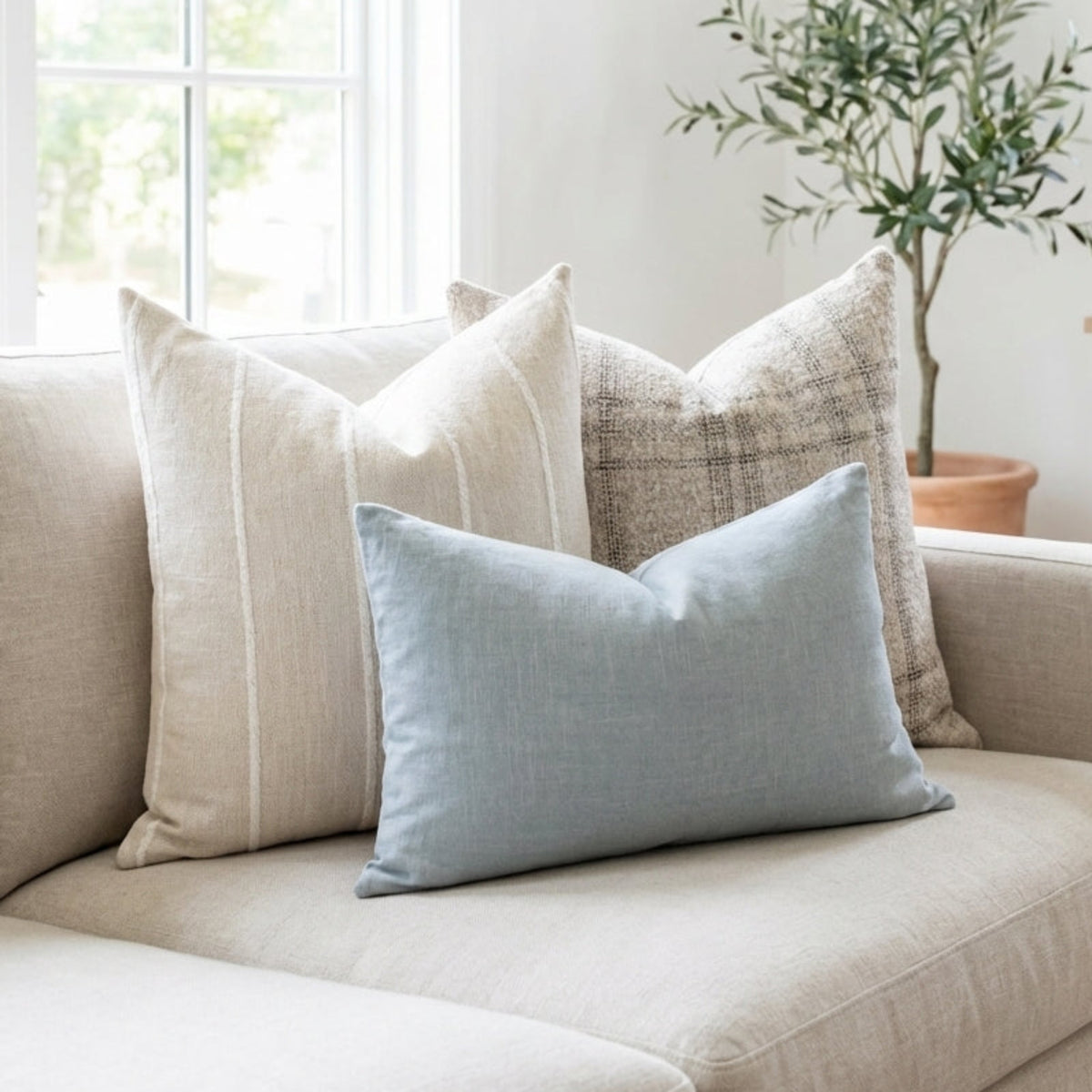 Stylish full-body shot of pillows on a cozy neutral sofa in a light, airy interior with soft daylight lighting and modern decor.