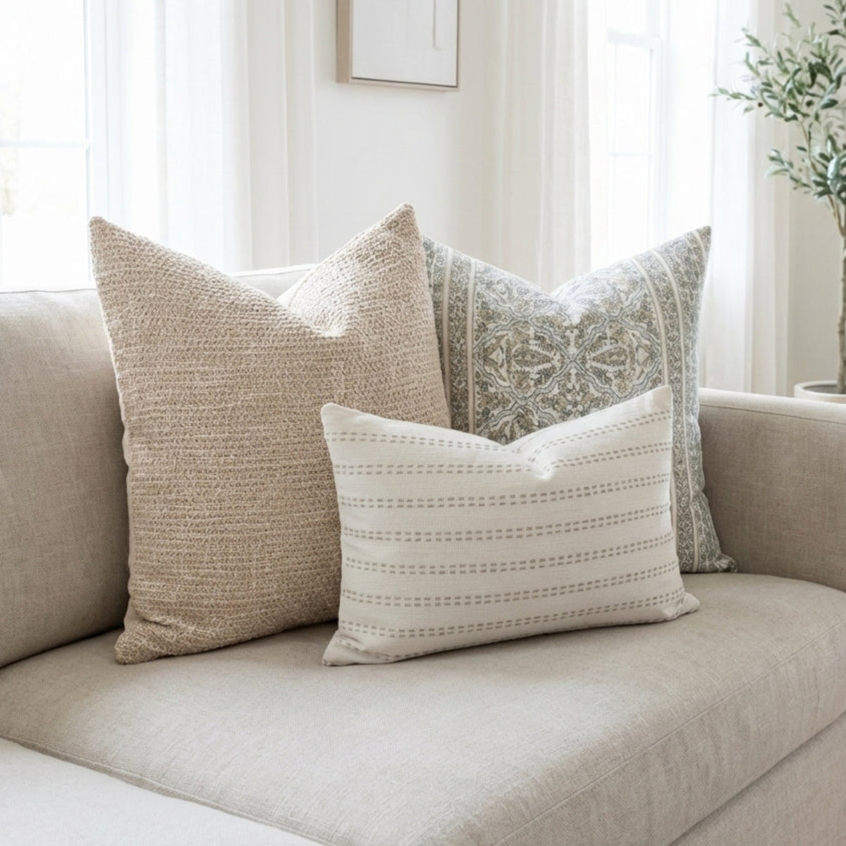 Full sofa view with Oversized Combo 8 pillows displaying floral, blush, and stripe patterns in a bright, minimalist living room setting.