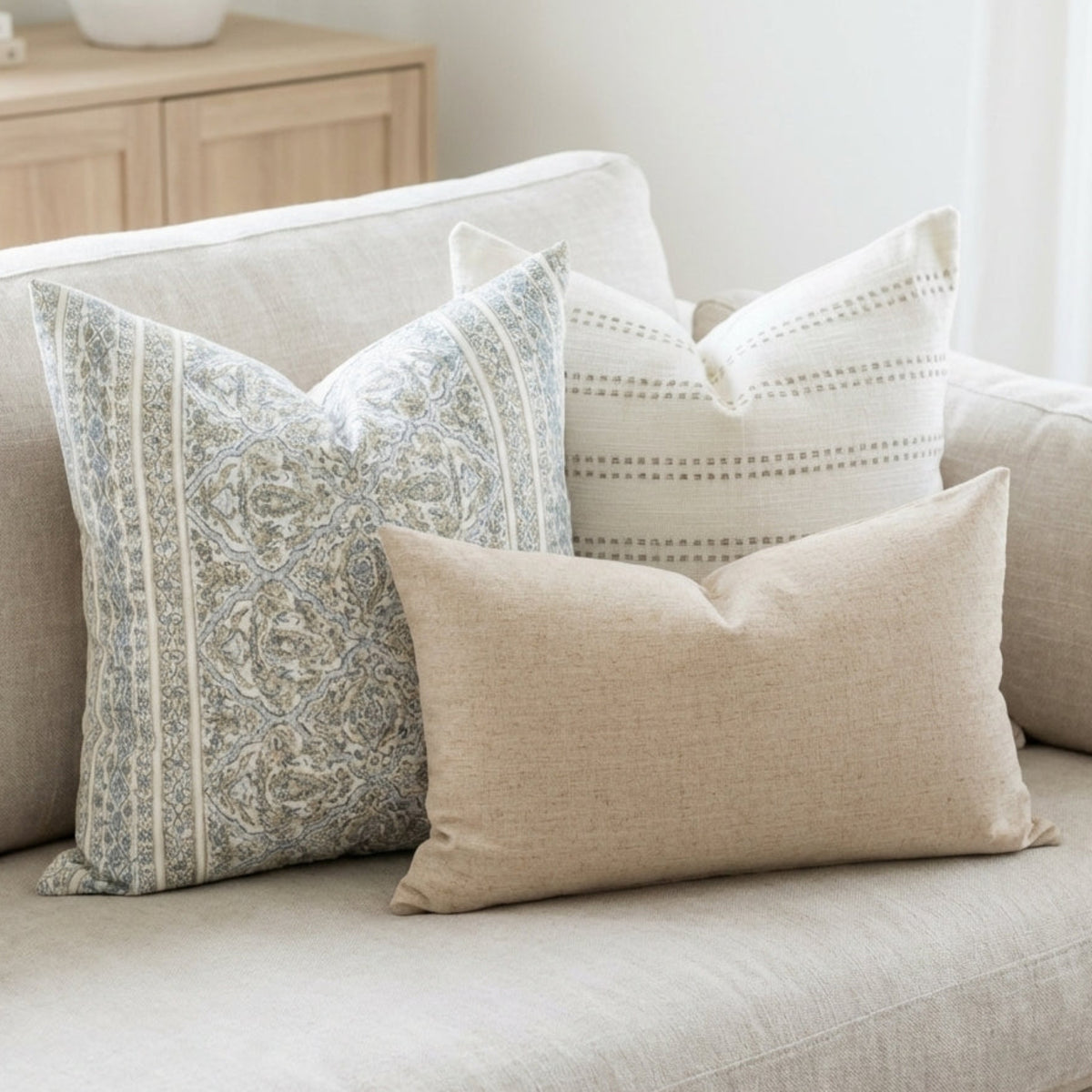 Full sofa view with three coordinated pillow covers, highlighting layered fabrics and refined textures in a bright, neutral living space.
