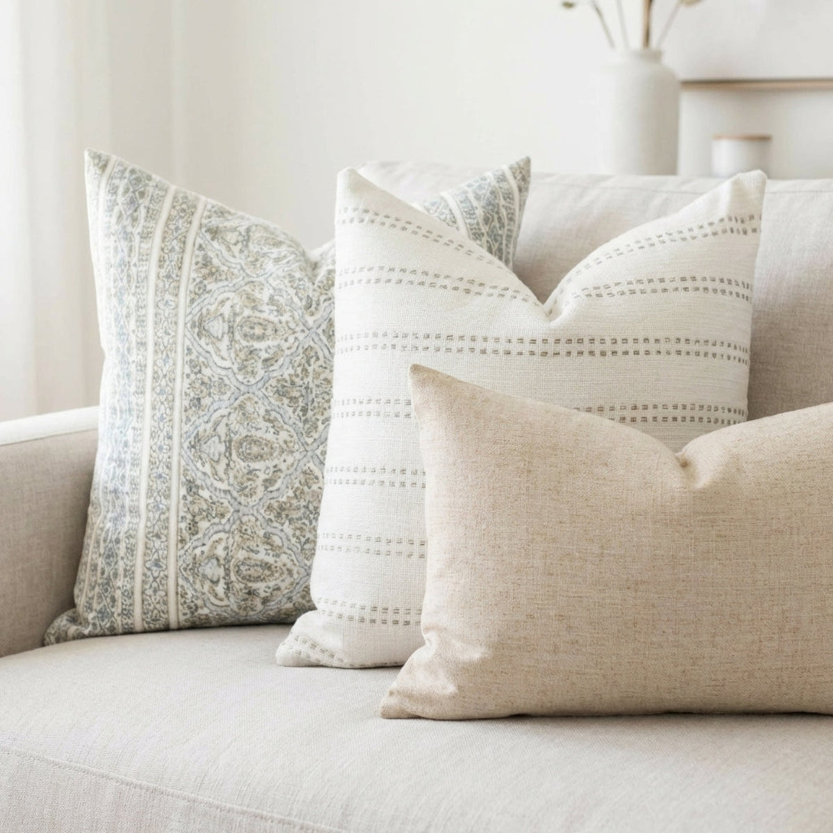 Set of three designer pillow covers on a neutral sofa, showcasing subtle patterns, stripes, and textures in an airy, sophisticated setting.