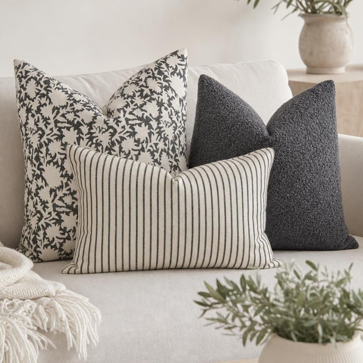 Set of three neutral pillow covers on a light sofa in a bright, airy living room, emphasizing cozy, layered decor.