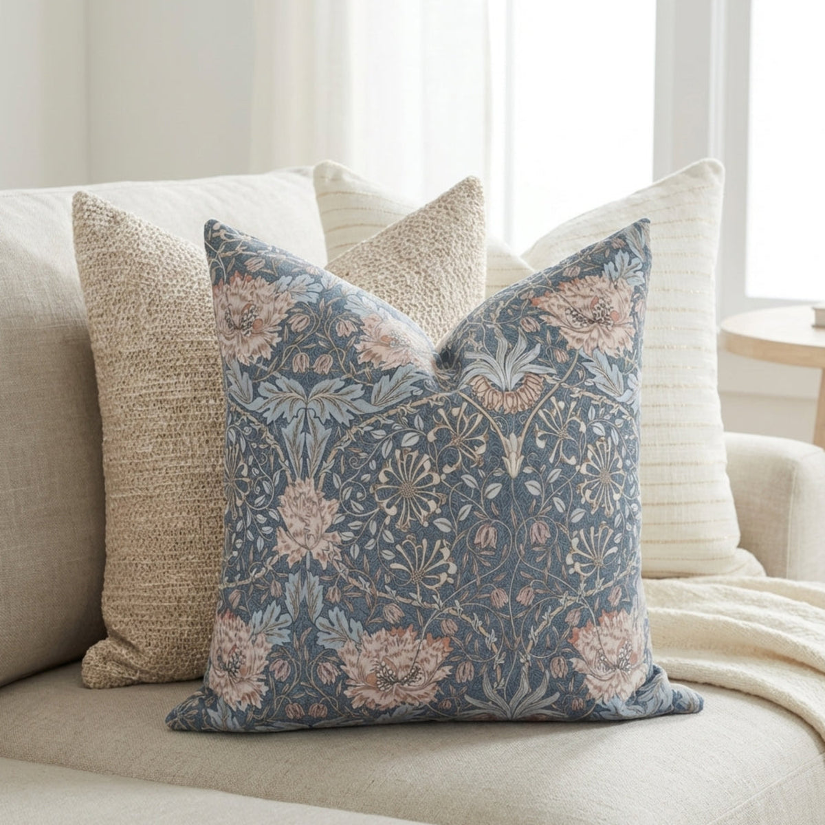 Three stylish pillows on a light sofa, featuring floral and striped patterns with textured fabrics in a calm, airy living space.