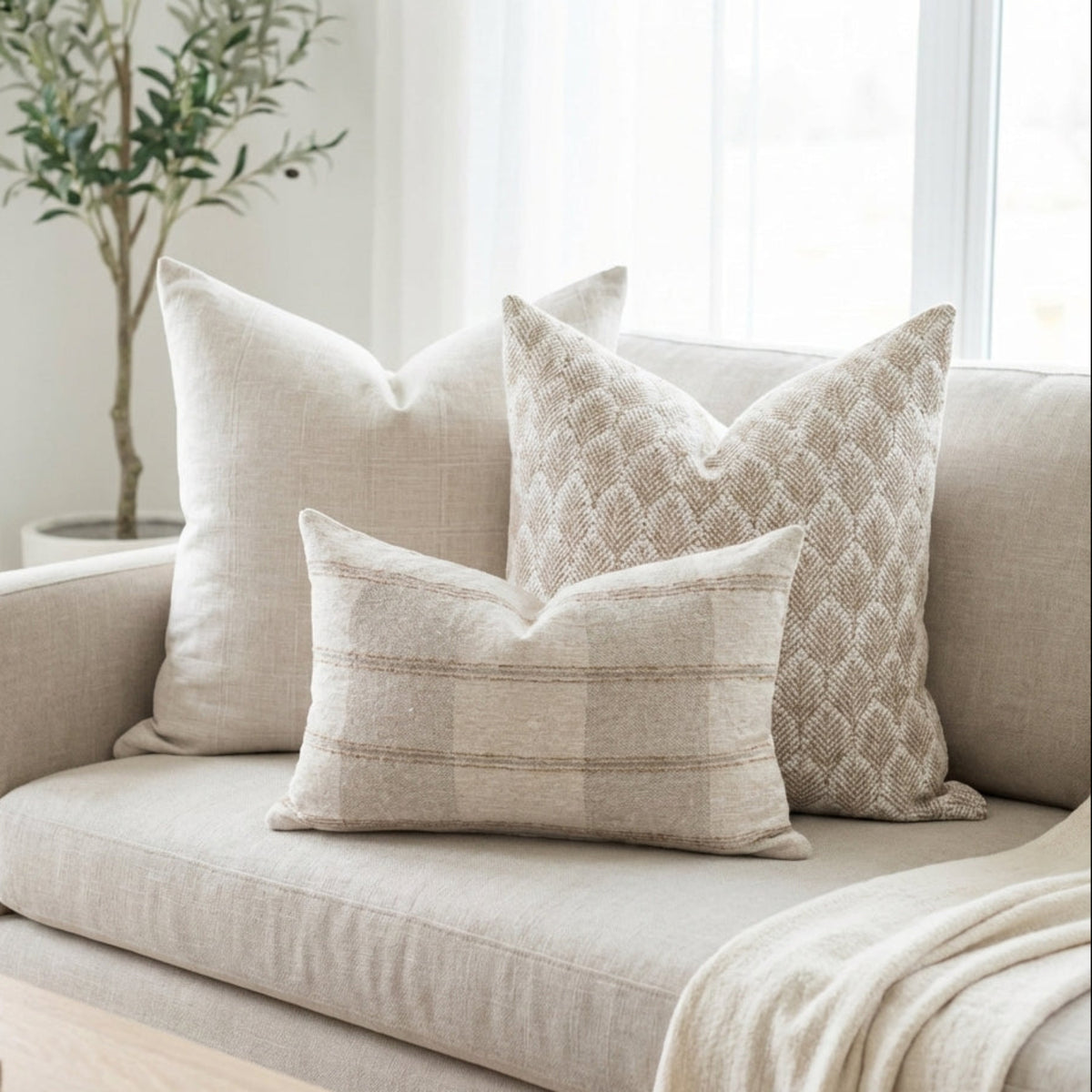 Full view of Oversized Combo 10 pillows arranged on a light sofa in a bright, airy living space highlighting their neutral colors and textures.