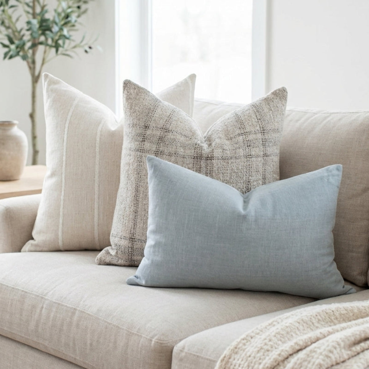 Photorealistic image of Ronan Sofa Combo 3 pillows on a neutral-toned sofa in a bright, airy living room with soft lighting and minimalist decor.