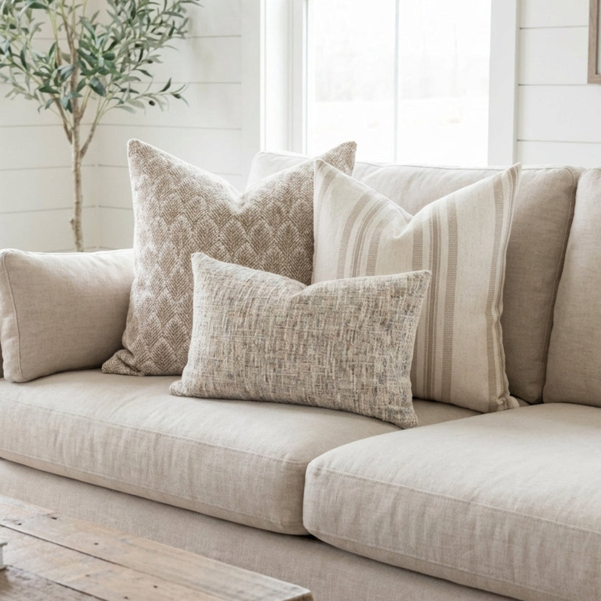 Full setup of Whitaker, Quincy, and Guinevere pillows casually styled on a plush sofa in a well-lit, modern farmhouse interior.